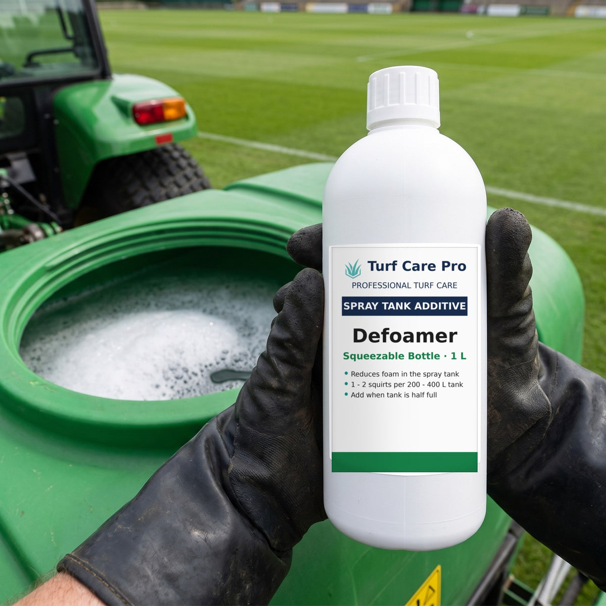 Gloved hands holding the squeezable defoamer bottle over a half-full sprayer tank with foam