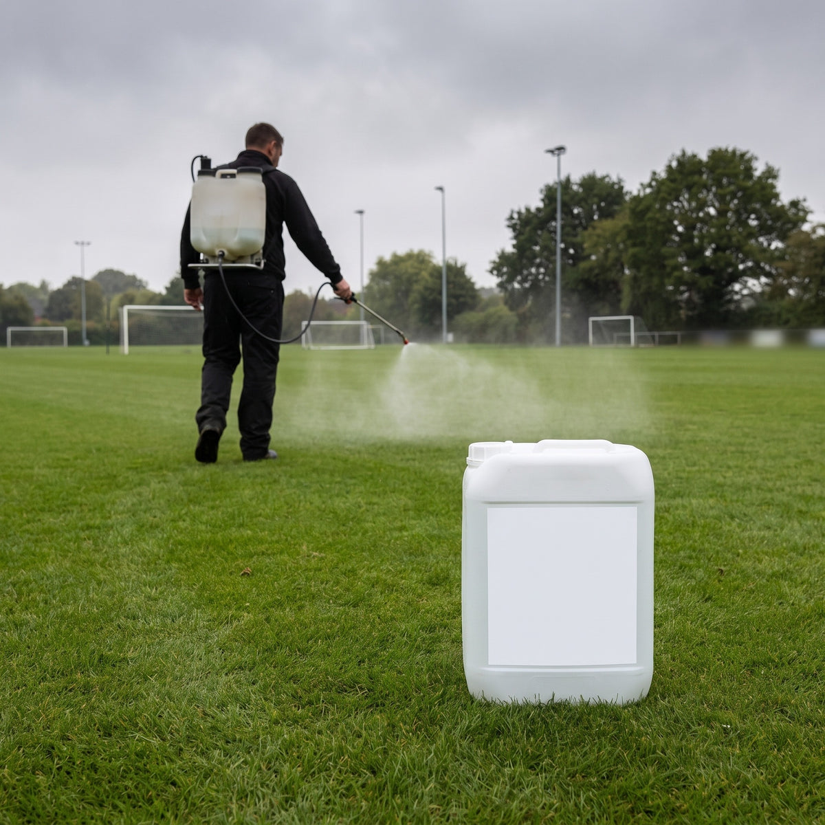 Groundsman applying liquid calcium turf hardener with a knapsack sprayer on a football pitch, 10L container in foreground